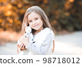Cute smiling baby girl 4-5 year old holding toy rabbit outdoors over nature background. Looking at camera. Childhood. 98718012