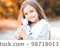 Smiling baby girl 4-5 year old holding handmade toy rabbit outdoors. Looking at camera. Childhood. 98718013