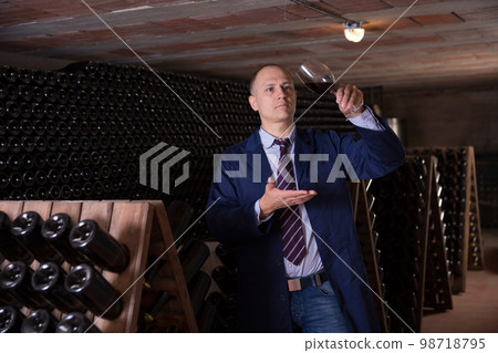 Wine producer inspecting quality of red wine in winery vault Wine producer inspecting quality of red wine in winery vault 98718795