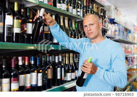 Focused male customer buying bottle of wine in supermarket Focused male customer buying bottle of wine in supermarket 98718903