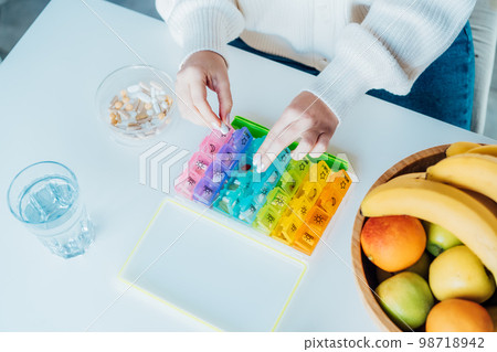 Woman's hands sorting pills into pills organizer. Close up medical pill box with daily doses of medicines. Antioxidant diet vitamin supplements for health and beauty care, biohacking concept. 98718942