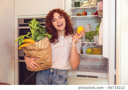 Ginger girl unpacking and putting food to the fridge Ginger girl unpacking and putting food to the fridge 98719222