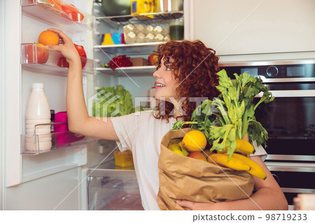 Ginger girl unpacking and putting food to the fridge 98719233