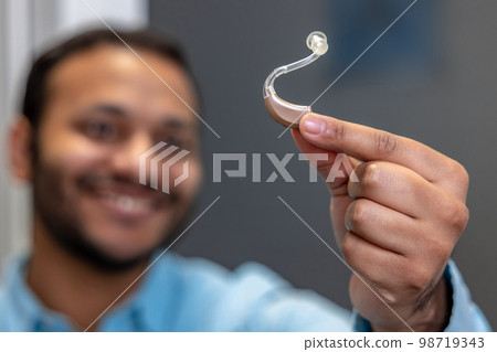 Smiling young man holding a hearing aid 98719343