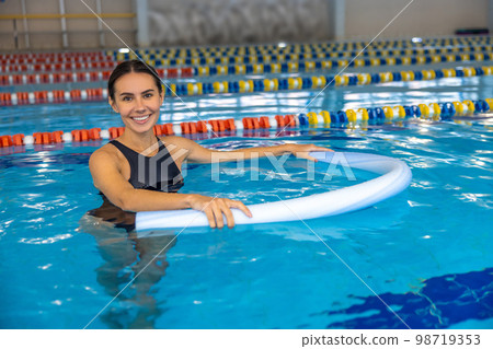 Smiling young woman doing exercises with float noodle 98719353