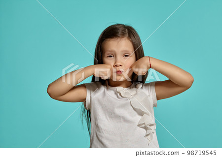 Close-up studio shot of beautiful brunette little girl posing against a blue background. Close-up studio shot of beautiful brunette little girl posing against a blue background. 98719545