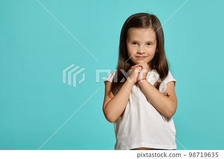 Close-up shot of a cute brunette little girl in a white blouse posing against a blue background. 98719635