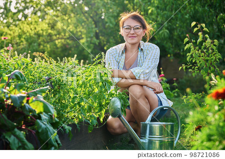 Middle-aged woman with watering can near garden bed with spicy fragrant herbs 98721086