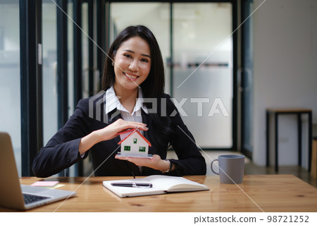 A real estate agent demonstrates the House model to clients interested in purchasing house insurance. The concept of home insurance and property A real estate agent demonstrates the House model to clients interested in purchasing house insurance. The concept of home insurance and property 98721252