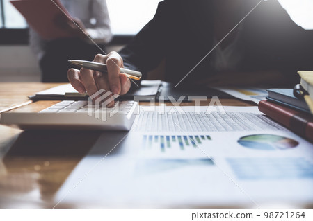Project management team updating and calculating financial chart on paperwork, two business people in office. 98721264