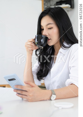 Portrait of Asian female business financial checking her port stock market in mobile application at morning with coffee. Portrait of Asian female business financial checking her port stock market in mobile application at morning with coffee. 98722016