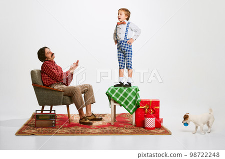 Saying poetry. Little boy, kid standing on chair and performing verse in front of his happy father applauding. Domestic lifestyle Saying poetry. Little boy, kid standing on chair and performing verse in front of his happy father applauding. Domestic lifestyle 98722248