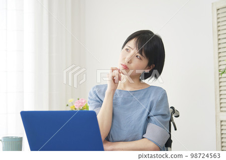 坐在輪椅上的殘疾婦女在家裡的電腦前思考 98724563