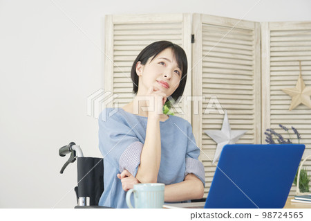 坐在輪椅上的殘疾婦女在家裡的電腦前想像 坐在輪椅上的殘疾婦女在家裡的電腦前想像 98724565