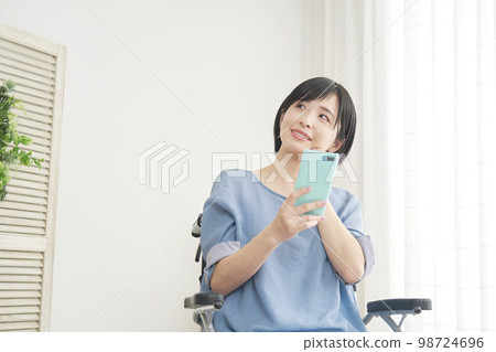 Disabled woman on a wheelchair thinking with a smartphone at home 98724696