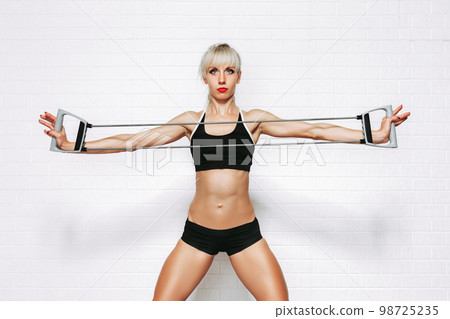 Slim young blond sportive woman doing exercises with expander while on white studio background Slim young blond sportive woman doing exercises with expander while on white studio background 98725235