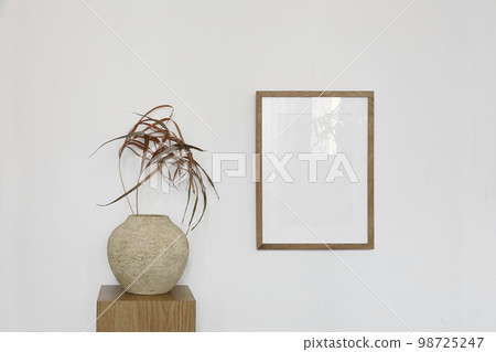 Boho artistic still life. Dry palm leaves in textured ceramic vase. Oak wooden podium, pedestal. Vertical picture frame mockup on white wall background. Empty artistic template. Minimal design. 98725247