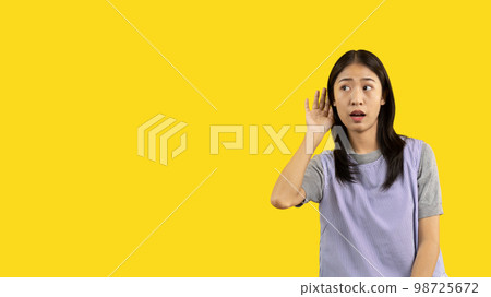 Asian woman eavesdropping or overhearing secret conversation isolated on yellow background, Gossip, Listening, Yellow background studio portrait. Asian woman eavesdropping or overhearing secret conversation isolated on yellow background, Gossip, Listening, Yellow background studio portrait. 98725672