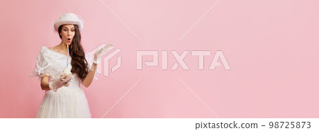 Portrait of beautiful lady in white vintage dress posing with birthday cake over pink background. Concept of 19th century, fashion, comparison of eras 98725873
