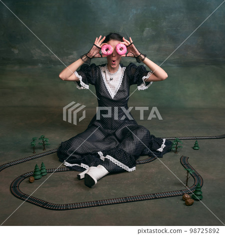 Sweets. Young beautiful woman in image of Anna Karenina in retro black dress posing with pink donuts over dark vintage background. Concept of literature character, history 98725892