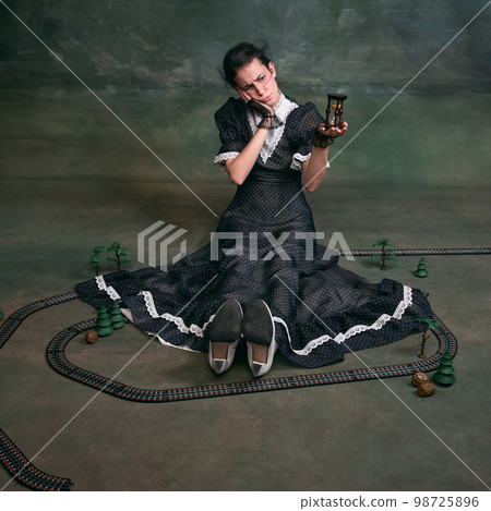 Waiting. Young beautiful woman in image of Anna Karenina in retro black dress posing around toy over dark vintage background. Concept of literature character, history 98725896