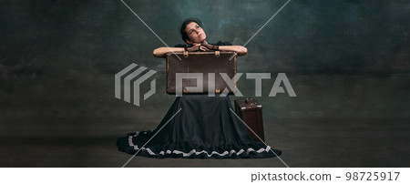 Arriving. Beautiful woman in image of Anna Karenina sitting on retro suitcase over vintage dark green background. Banner. Concept of literature character, history Arriving. Beautiful woman in image of Anna Karenina sitting on retro suitcase over vintage dark green background. Banner. Concept of literature character, history 98725917