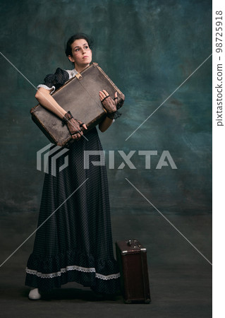 Holding suitcase. Destiny. Beautiful woman in image of Anna Karenina over vintage dark green background. Concept of literature character, history Holding suitcase. Destiny. Beautiful woman in image of Anna Karenina over vintage dark green background. Concept of literature character, history 98725918