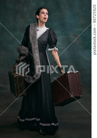 Emotions. Beautiful woman in image of Anna Karenina with retro suitcases over vintage dark green background. Concept of literature character, history Emotions. Beautiful woman in image of Anna Karenina with retro suitcases over vintage dark green background. Concept of literature character, history 98725920