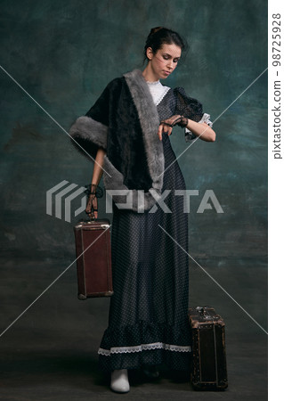 Travelling. Time. Beautiful woman in image of Anna Karenina with retro suitcases over vintage dark green background. Concept of literature character, history Travelling. Time. Beautiful woman in image of Anna Karenina with retro suitcases over vintage dark green background. Concept of literature character, history 98725928