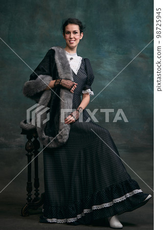 Beautiful woman in image of Anna Karenina in stylish dark dress posing over vintage dark green background. Concept of literature character, history Beautiful woman in image of Anna Karenina in stylish dark dress posing over vintage dark green background. Concept of literature character, history 98725945