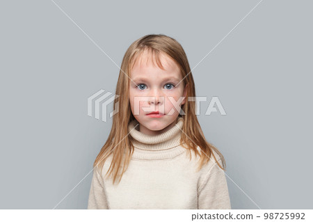 Portrait of serious funny little girl looking at camera on grey background Portrait of serious funny little girl looking at camera on grey background 98725992