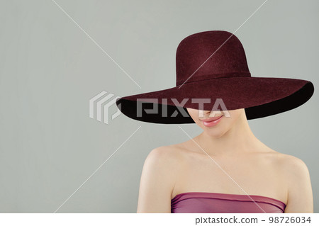 Beautiful young happy woman with clean fresh skin in burgundy wide hat on ligth grey background 98726034