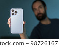 a young man shows a smartphone to the camera 98726167