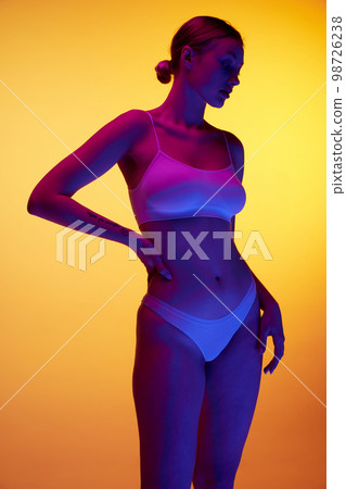Silhouette of beautiful slim woman wearing underwear over orange studio background in purple neon light. Concept of beauty, body and skin care, health, plastic surgery, cosmetics Silhouette of beautiful slim woman wearing underwear over orange studio background in purple neon light. Concept of beauty, body and skin care, health, plastic surgery, cosmetics 98726238