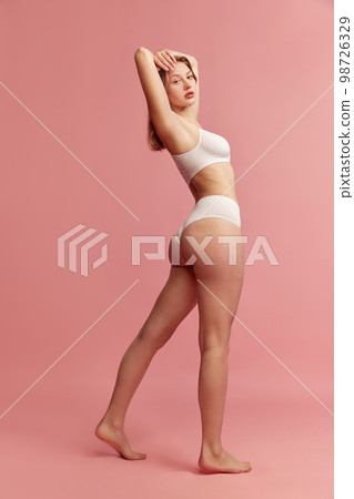 Studio shot of young slim woman wearing white inner wear posing over pink color background. Concept of natural beauty, body and skin care, healthy eating 98726329