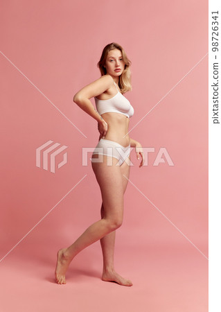 Studio shot of young slim woman wearing white inner wear posing over pink color background. Concept of natural beauty, body and skin care, healthy eating 98726341