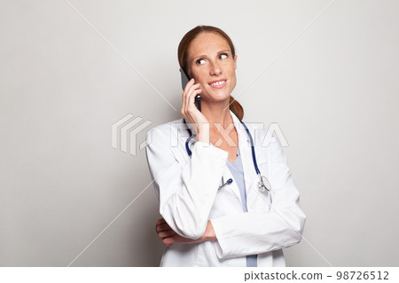 Beautiful doctor mid adult woman wearing white medical uniform using smartphone 98726512