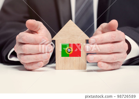 Businessman hand holding wooden home model with Portugese flag. insurance and property concepts Businessman hand holding wooden home model with Portugese flag. insurance and property concepts 98726589