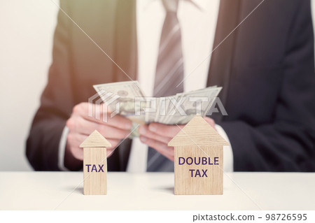 Wooden houses with words tax and double tax, business tax concept, us dollars money in hands Wooden houses with words tax and double tax, business tax concept, us dollars money in hands 98726595