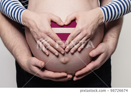 Latvian family concept. Man embracing pregnant woman belly and heart with flag of Latvia Latvian family concept. Man embracing pregnant woman belly and heart with flag of Latvia 98726674