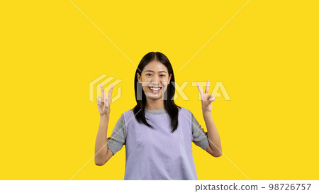 Young Asian woman making two thumbs up gesture showing joy and fun, Symbol of good friendship, Popular photo poses, Make a v-shaped finger, Yellow background. Young Asian woman making two thumbs up gesture showing joy and fun, Symbol of good friendship, Popular photo poses, Make a v-shaped finger, Yellow background. 98726757