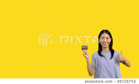 Asian woman holding credit card and thumbs up on yellow background, Suggest or demonstrate the use of credit cards instead of cash, Payment, Finance, Transact or spend online. 98726758