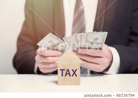 Wooden house with word tax, business tax, big taxes concept, us dollars banknotes Wooden house with word tax, business tax, big taxes concept, us dollars banknotes 98726794