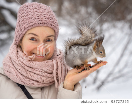 Girl feeds a squirrel with nuts at winter. Caring for animals in winter or autumn. 98727235