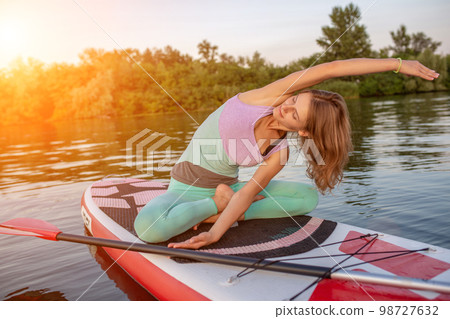 Young beautiful woman meditating in a sea at SUP paddleboarding. Healthy lifestyle. 98727632