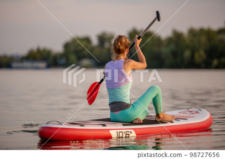 Sporty woman in yoga position on paddleboard, doing yoga on sup board, exercise for flexibility and stretching of muscles 98727656