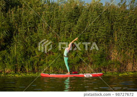 Young woman are doing yoga on a stand up paddle board SUP on a beautiful lake or river 98727672