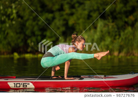 Young woman are doing yoga on a stand up paddle board SUP on a beautiful lake or river 98727676