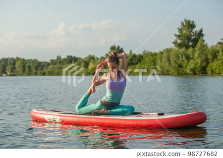 Young woman doing yoga on sup board with paddle. Meditative pose, side view - concept of harmony with the nature 98727682
