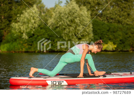 Woman practicing yoga on the paddle board in the morning Woman practicing yoga on the paddle board in the morning 98727689